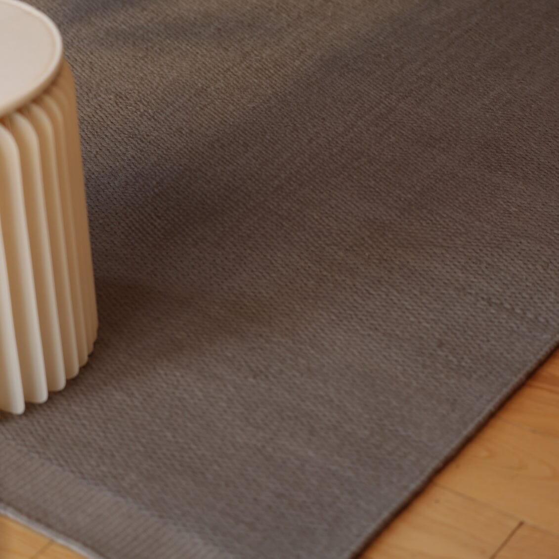 Slate Gray wool rug on a wooden floor with a beige cylindrical object to the left. #slategray