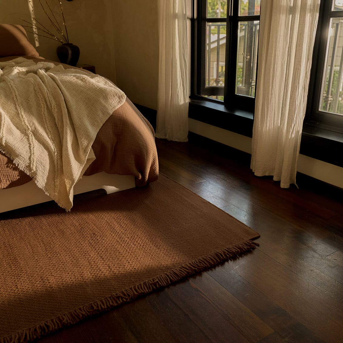 Bedroom with wooden floor, bed, and large windows with curtains. #sunsettan