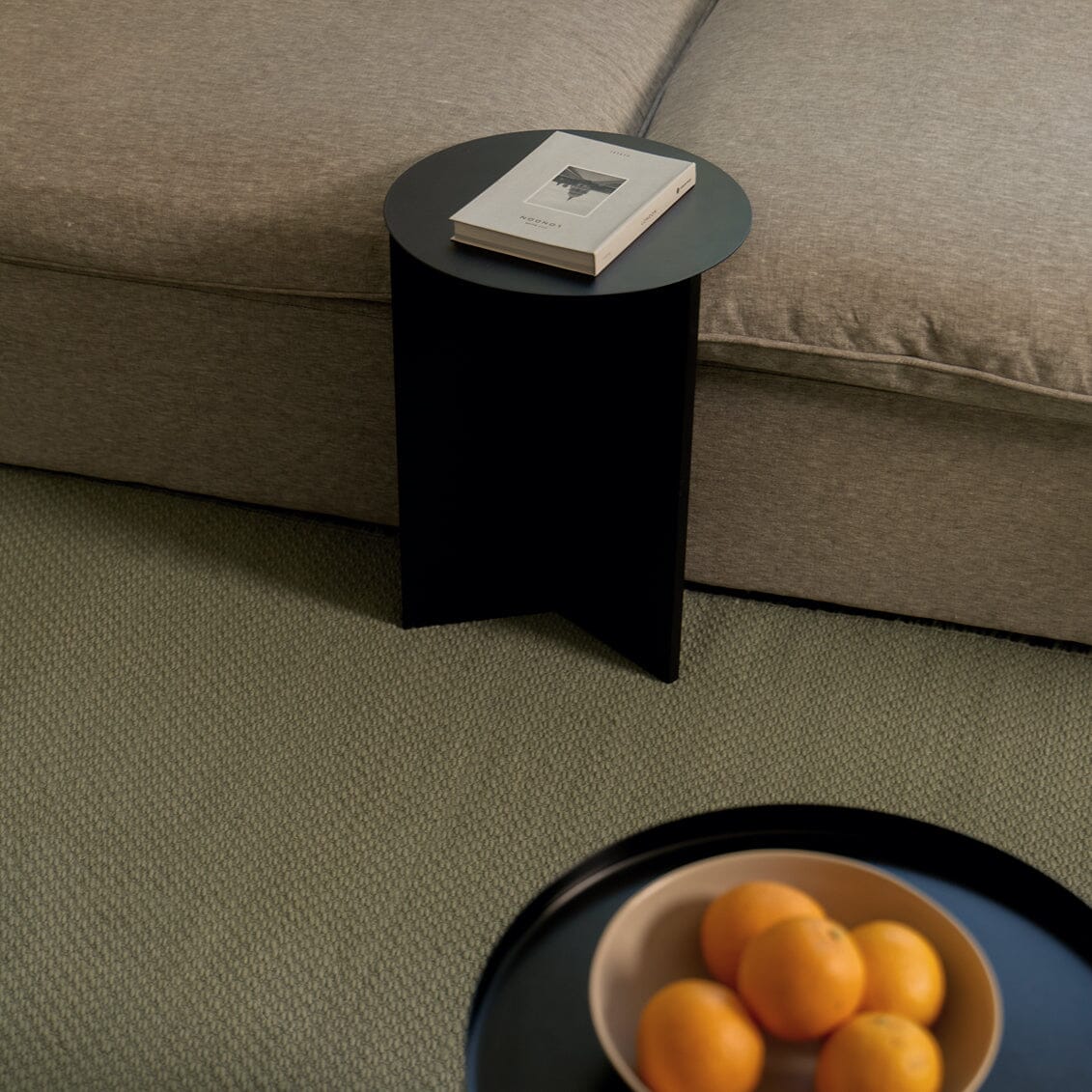 Black side table next to a beige sofa with a book on top, and a bowl of oranges on the floor. #sagegreen