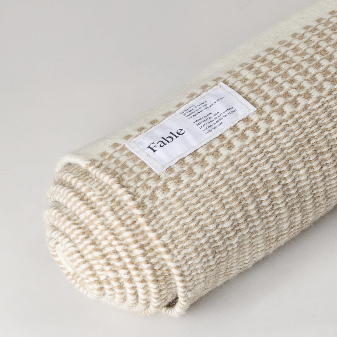 Rolled-up beige blanket with a label on a light gray background #coastalcream