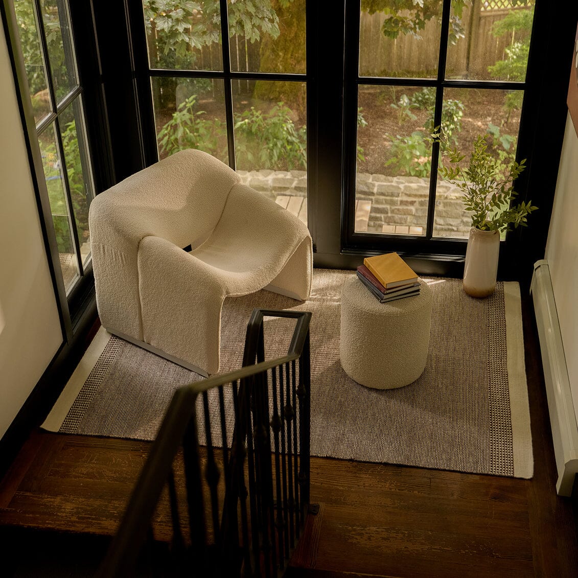Modern living room with a beige armchair, small table, and decorative items near large windows. #burntsienna