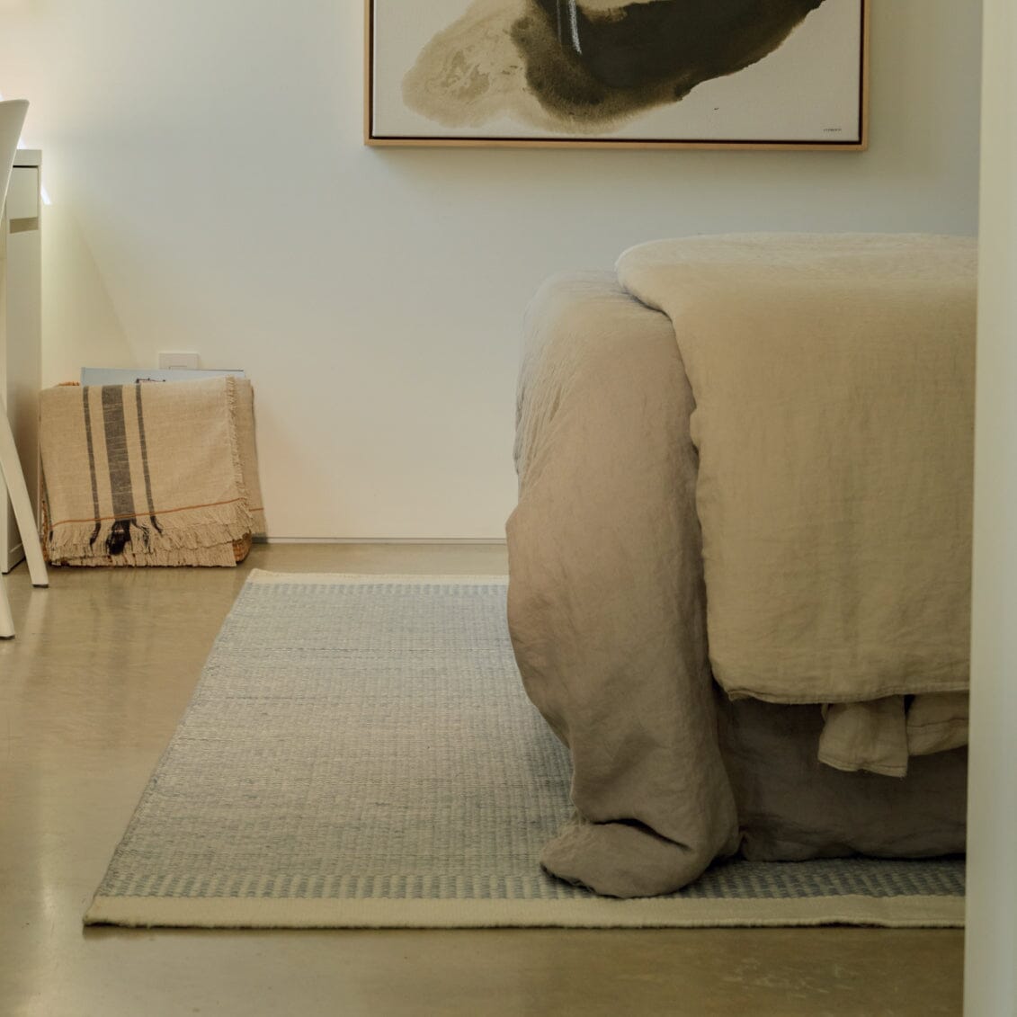 Beige bedspread on a bed in a room with a rug and wall art. #duskblue