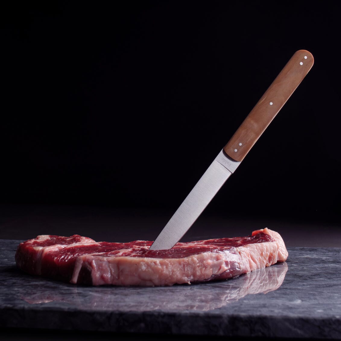Raw steak with a knife on a dark surface
