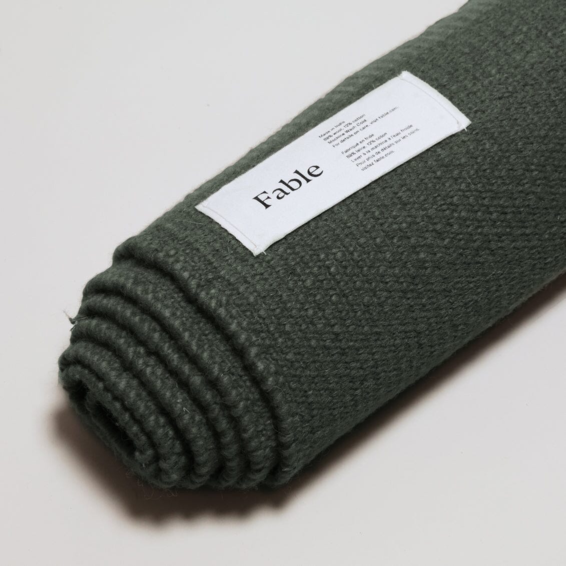 Rolled-up green blanket with a 'Fable' label on the shoreline green wool rug background. #forestgreen