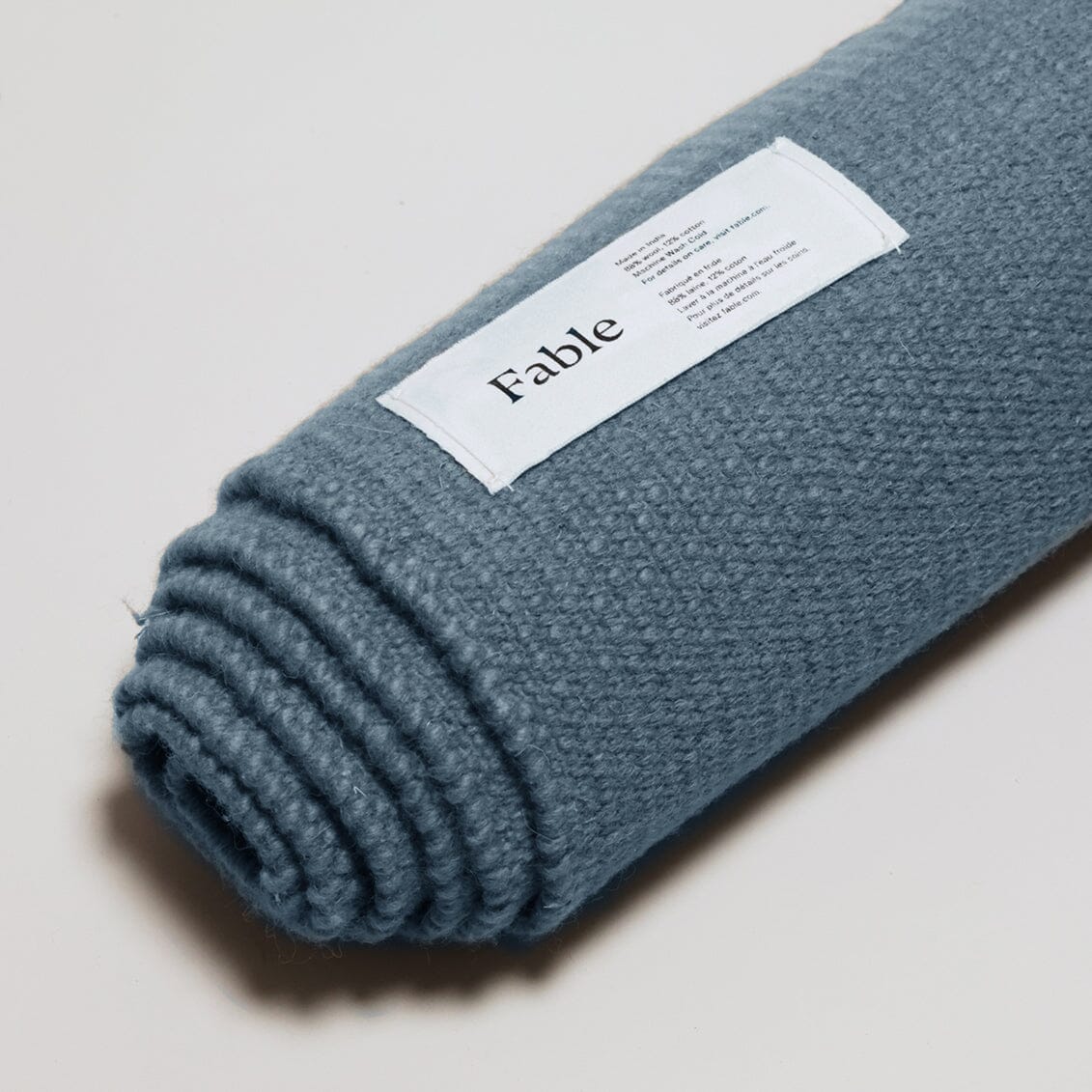 Rolled-up Seaside blue rug with a 'Fable' label on the gray background. #seasideblue
